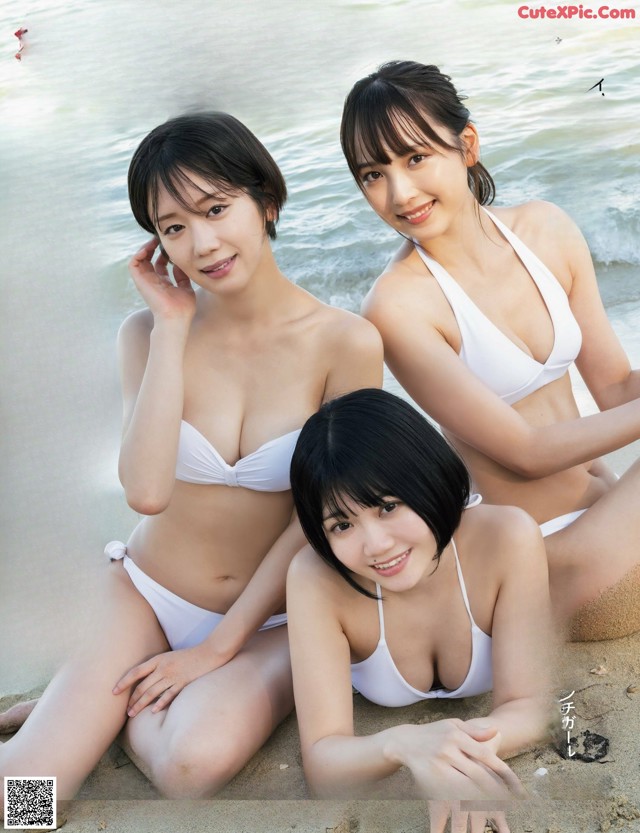 A group of three women in bikinis sitting on the beach.