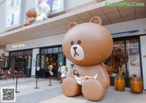 A woman pushing a shopping cart next to a giant teddy bear.