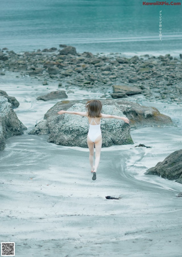 A woman in a white bathing suit running on the beach.