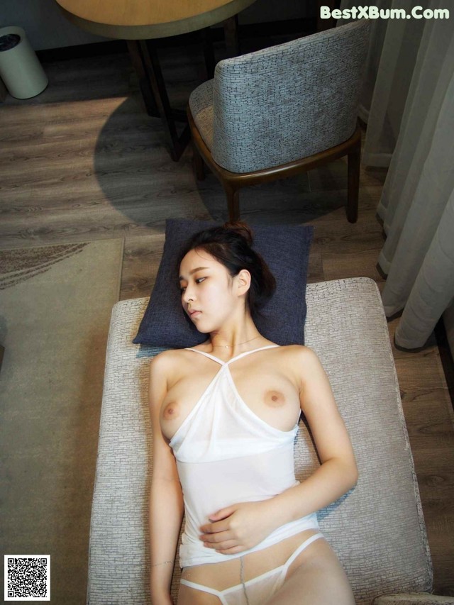 A woman in a white tank top laying on a couch.