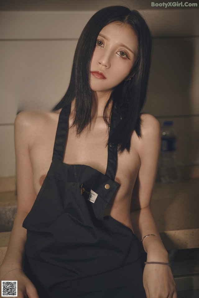 A woman in a black apron sitting on a kitchen counter.