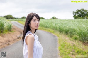 A woman in a white dress standing on the side of a road.