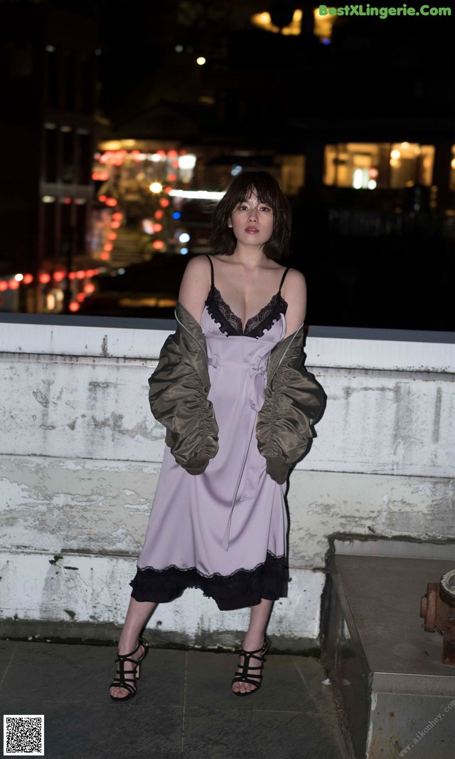 A woman in a pink dress and jacket standing on a ledge.