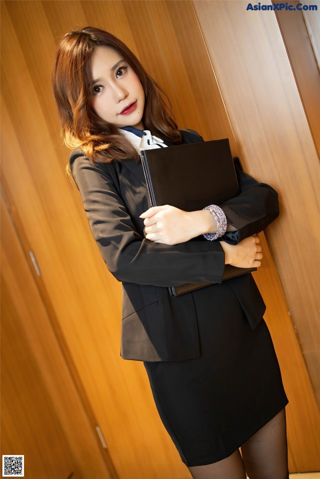 A woman in a business suit leaning against a wall.