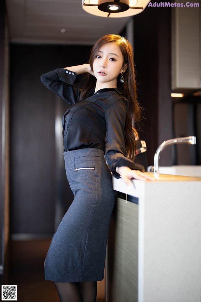 A woman in a black shirt and gray skirt leaning against a counter.