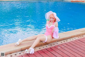 A woman in a pink bathing suit and a white hat by a pool.