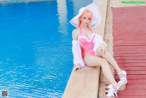 A woman in a pink bikini and a white hat sitting by a pool.