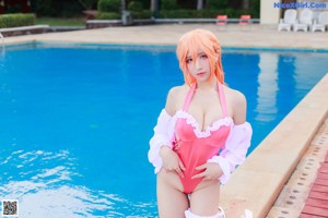 A woman in a pink bathing suit and white hat sitting by a pool.