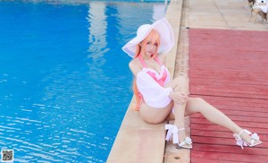A woman in a pink bikini and a white hat sitting by a pool.