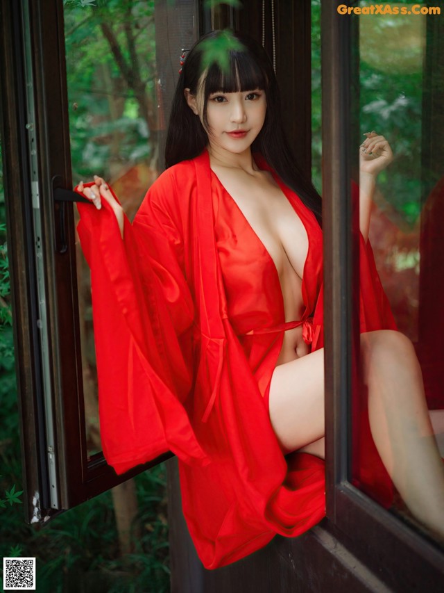 A woman in a red robe sitting on a window sill.