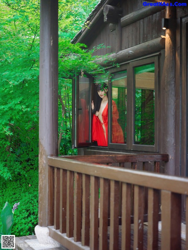 A woman in a red dress standing in the window of a cabin.