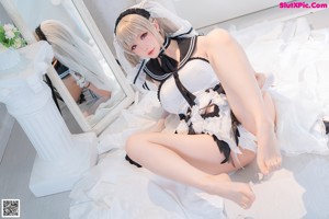 A woman in a maid outfit sitting on a bed.