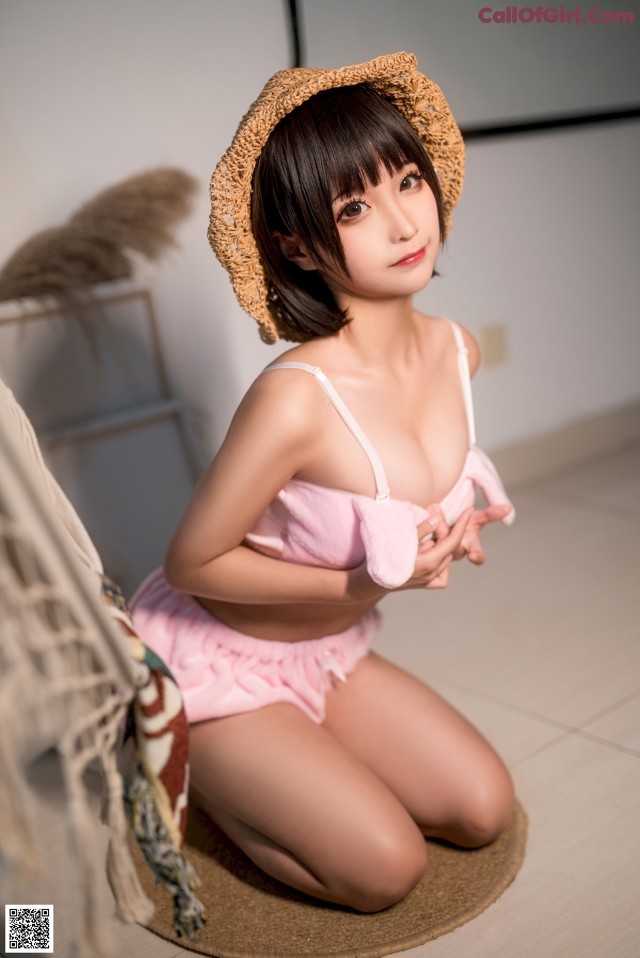 A woman in a pink bikini and a straw hat sitting on the floor.