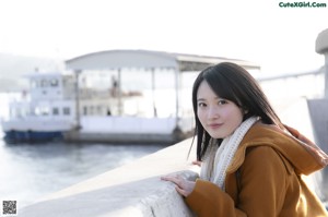 A woman in a brown coat standing by the water.