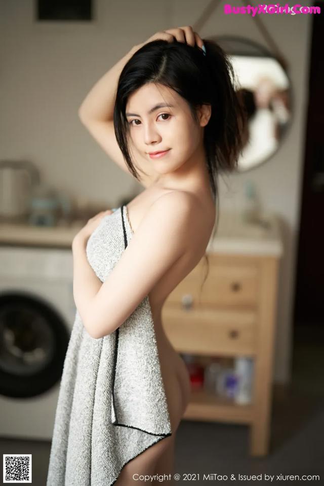 A woman in a towel standing in front of a washing machine.