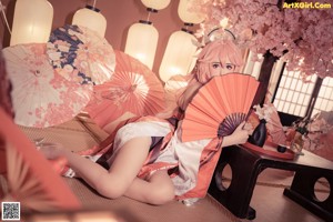 A woman in a kimono sitting on the floor with an umbrella.