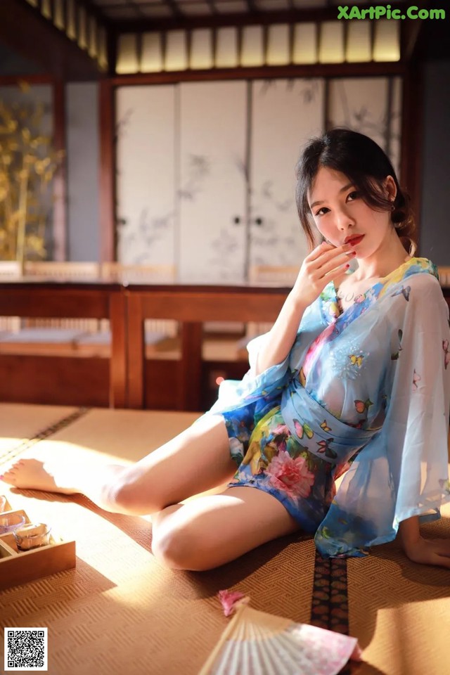 A woman in a blue kimono sitting on a tatami mat.