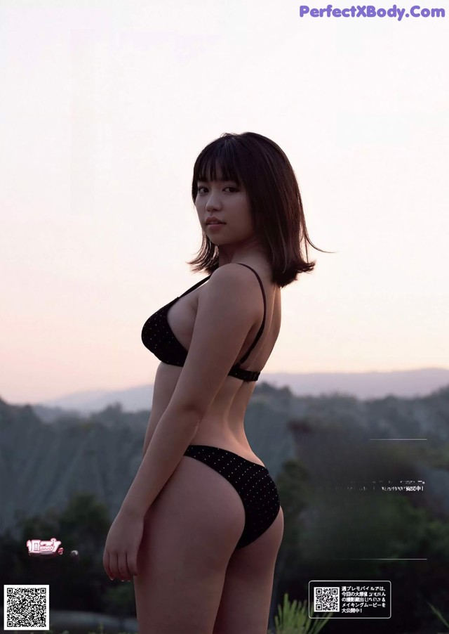 A woman in a black bikini standing in a field.