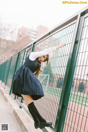 A woman in a school uniform leaning against a window.