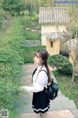 A woman in a school uniform leaning against a fence.