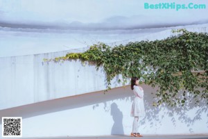 A woman in a white dress standing in front of a white wall.
