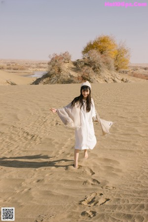 A woman in a white dress standing in the sand.