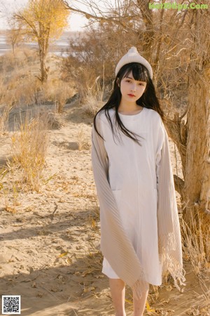 A woman in a white dress and hat sitting in the sand.