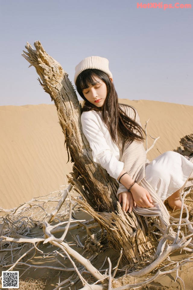 A woman sitting on top of a tree in the desert.