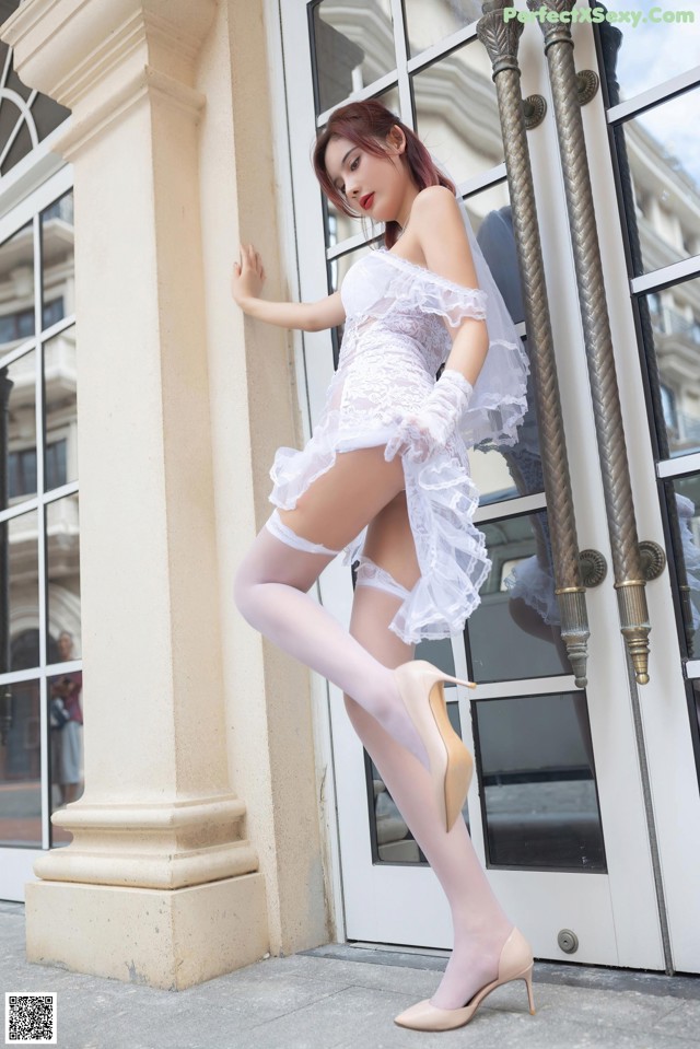 A woman in a white dress and stockings leaning against a door.