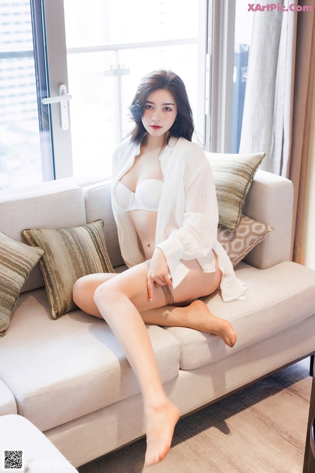 A woman sitting on a couch in a white lingerie.