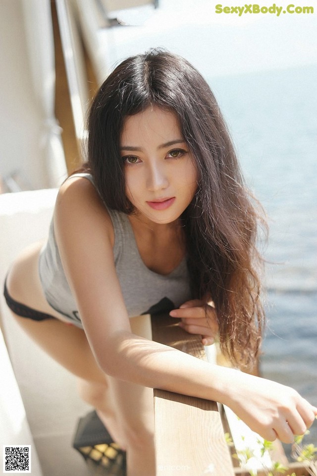 A woman in a gray tank top and black panties leaning on a railing.