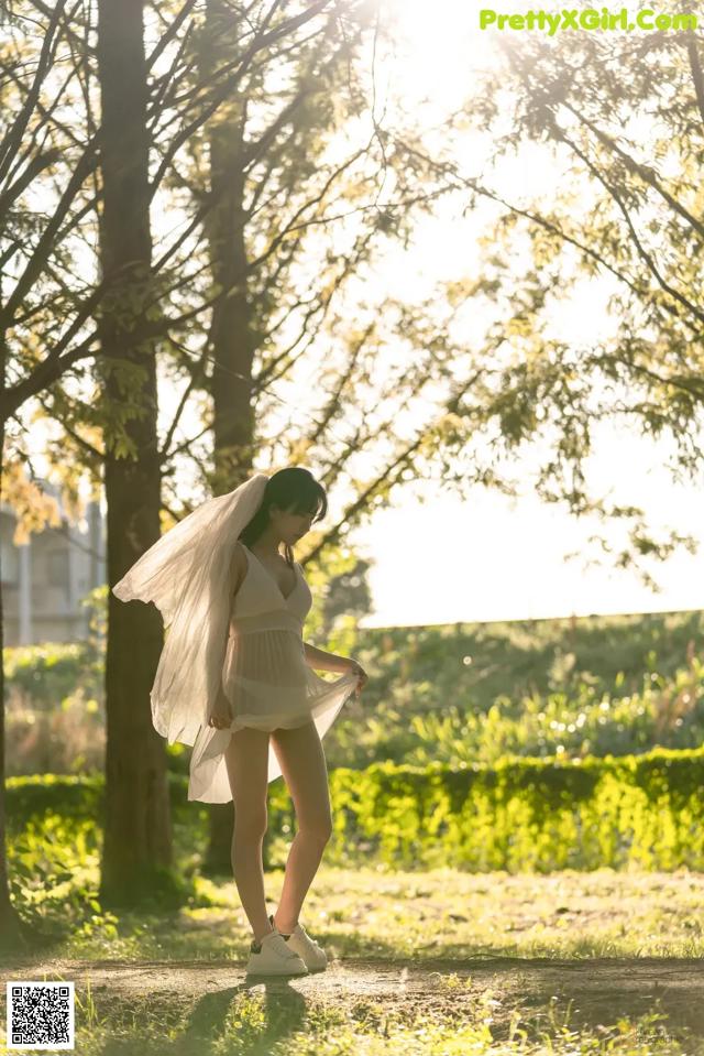 A woman in a white dress standing in a park.