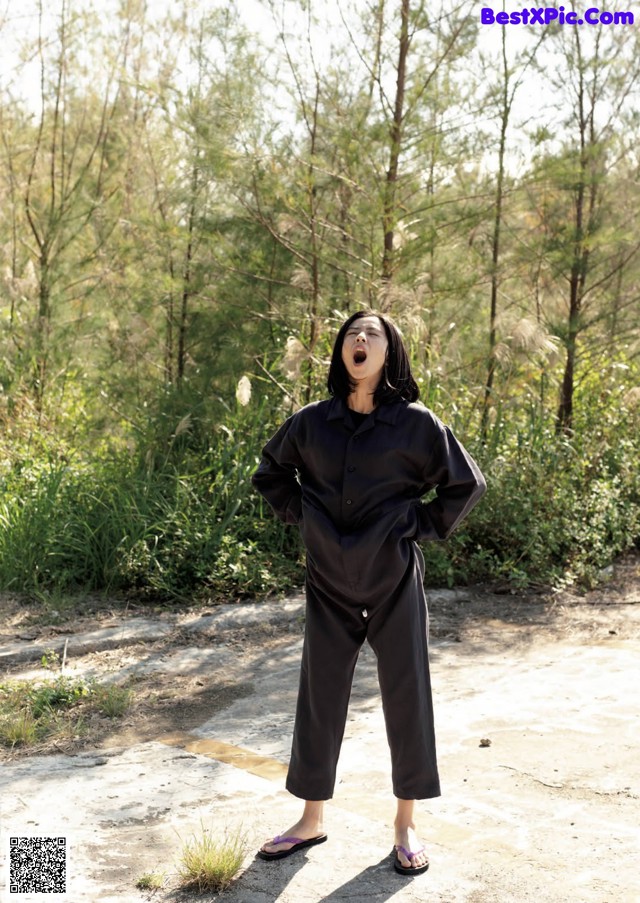 A woman standing in the middle of a dirt road.