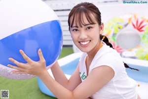 A woman in a white shirt and yellow bikini holding a beach ball.