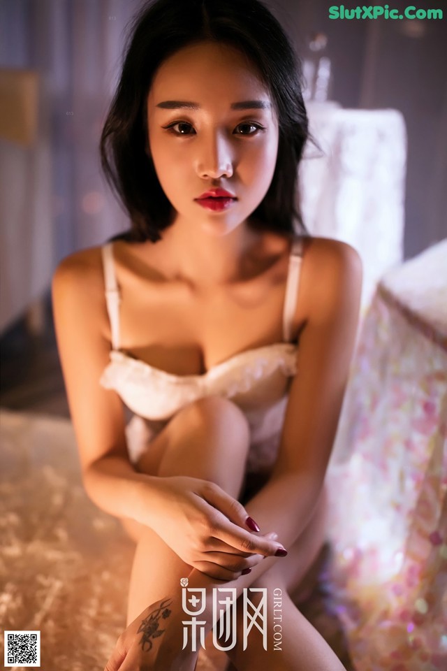 A woman in a white lingerie sitting on a bed.