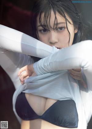 A woman in a gray tank top leaning against a white curtain.