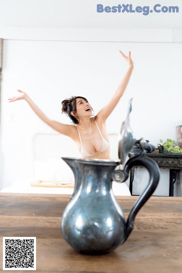 A woman in a white bra top standing next to a silver pitcher.