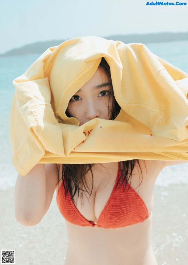 A woman in a bikini holding a yellow towel over her head.