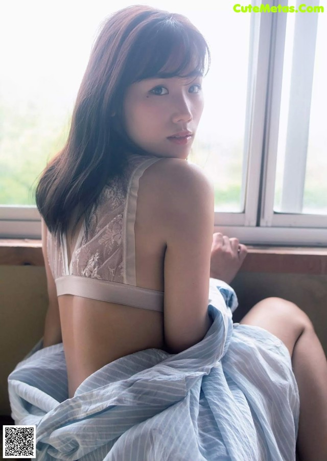 A woman sitting on a window sill in a white bra.