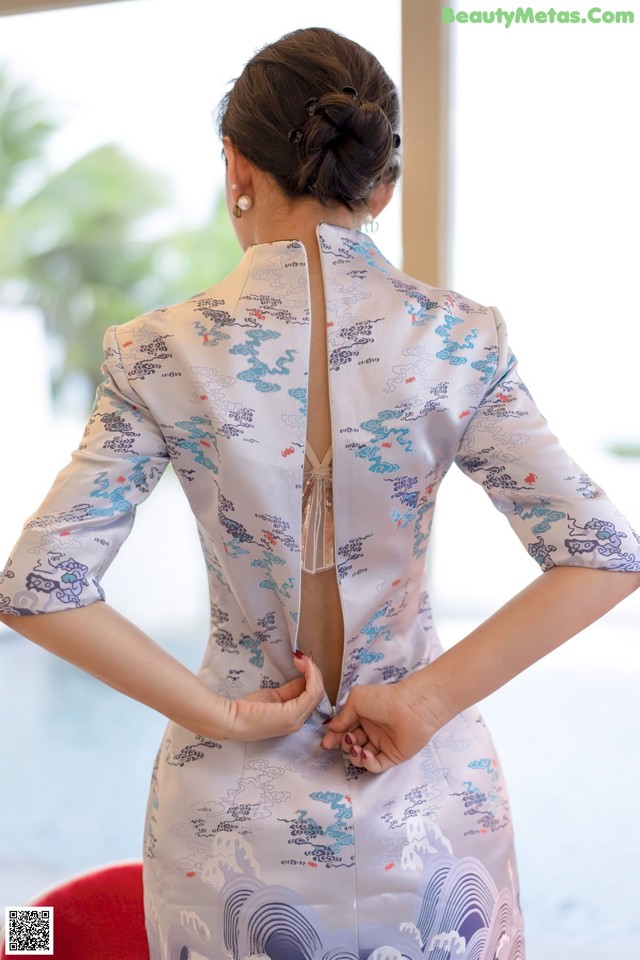 A woman in a blue and white cheongsam with her back to the camera.