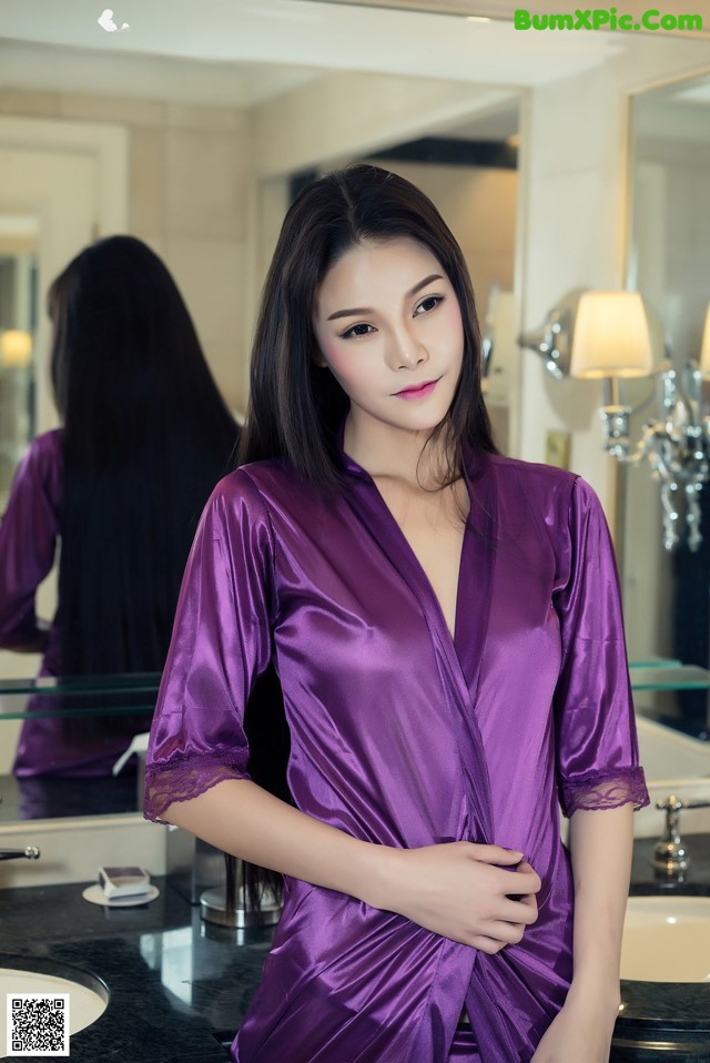 A woman in a purple robe standing in front of a mirror.