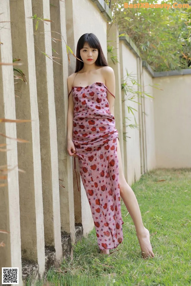 A woman in a pink dress leaning against a wall.