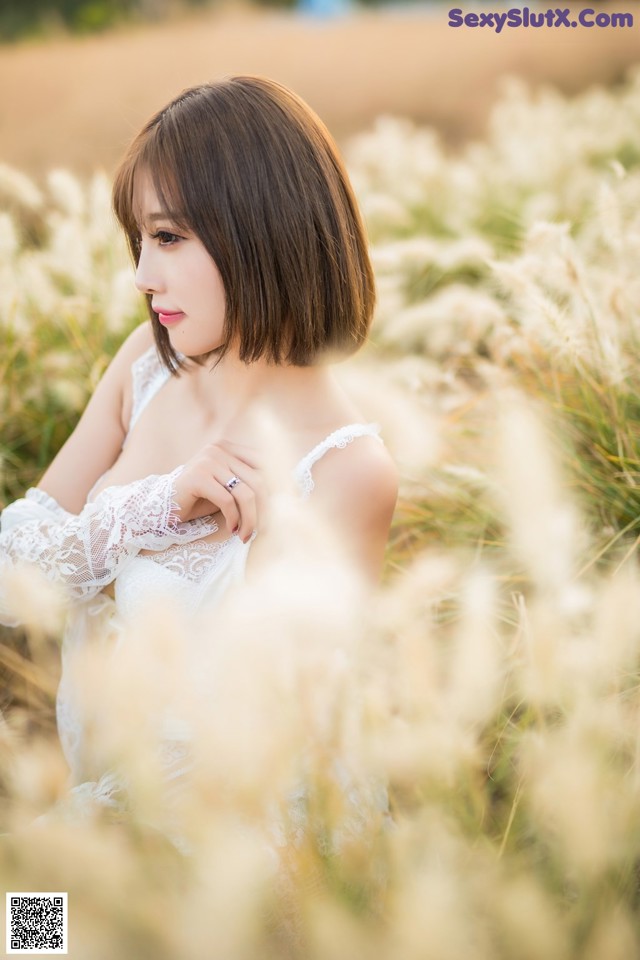 A woman in a white dress sitting in a field of tall grass.