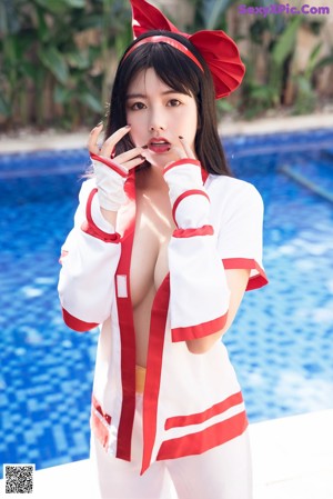 A naked asian woman in a red and white outfit next to a pool.