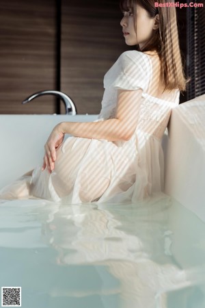 A woman in a white dress sitting in a bathtub.