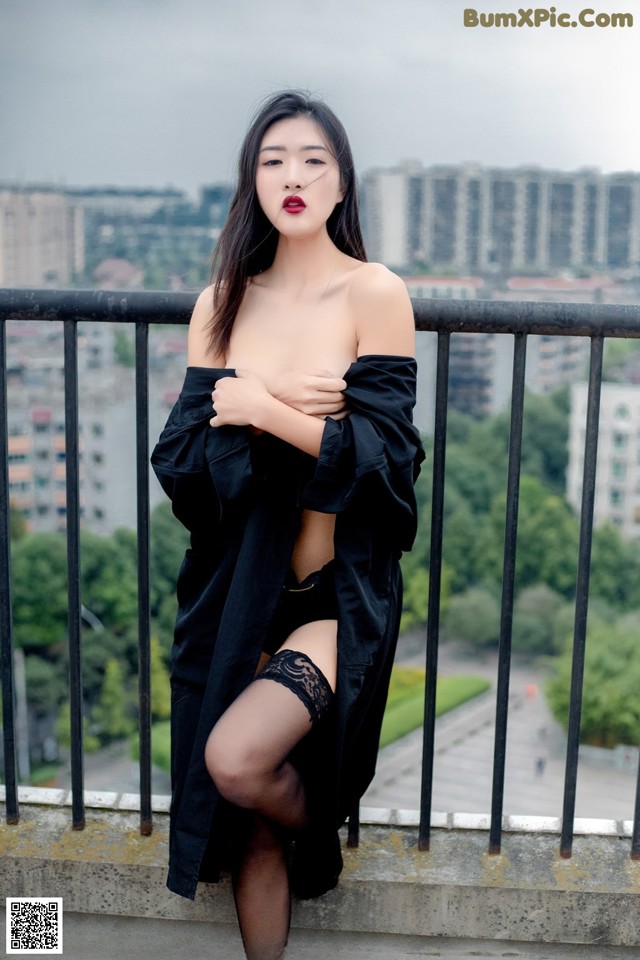 A woman in a black dress and stockings posing on a balcony.