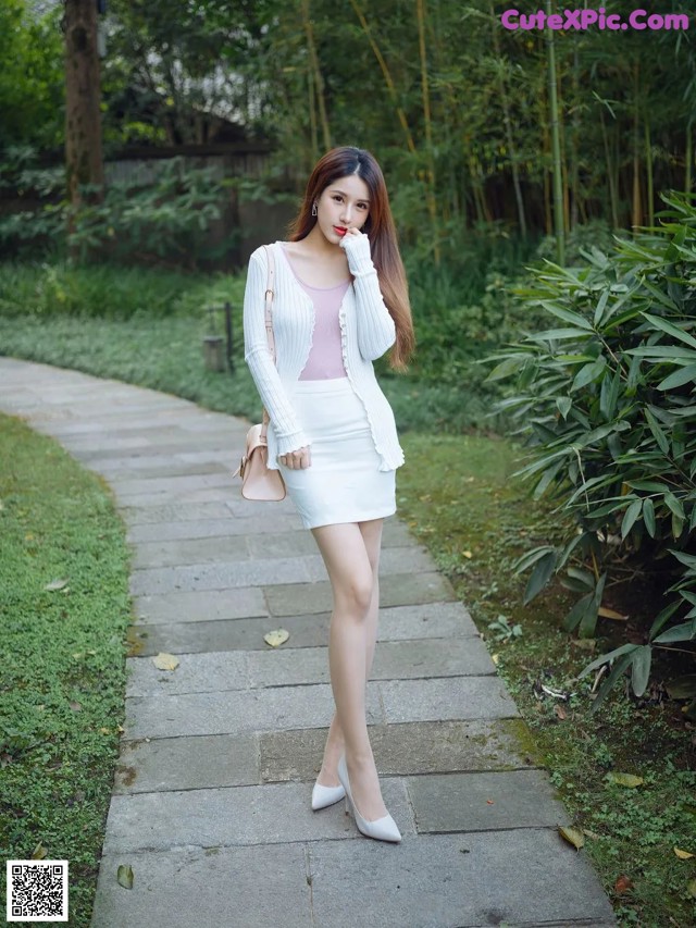 A woman in a white skirt and a pink top is walking down a path.