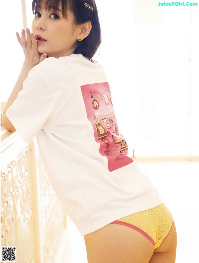 A woman in a white shirt and yellow panties posing for a picture.