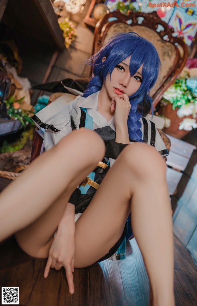 A woman with blue hair sitting on a wooden floor.